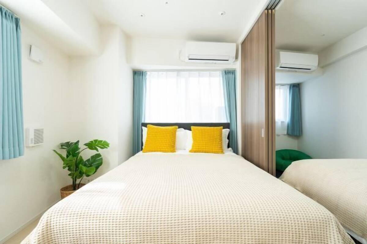 A hotel room with a large bed, two air conditioning units, a potted plant, and a green chair.