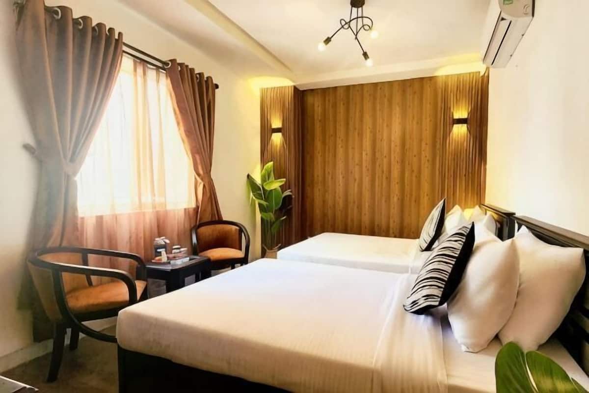 Une chambre d’hôtel avec un lit, deux chaises, une petite table et une plante.