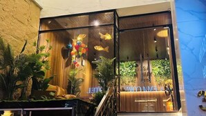 A hotel lobby with a wooden reception desk, glass partitions, and indoor plants. - RosaMay Thu Khoa Huan (Ho Chi Minh City)
