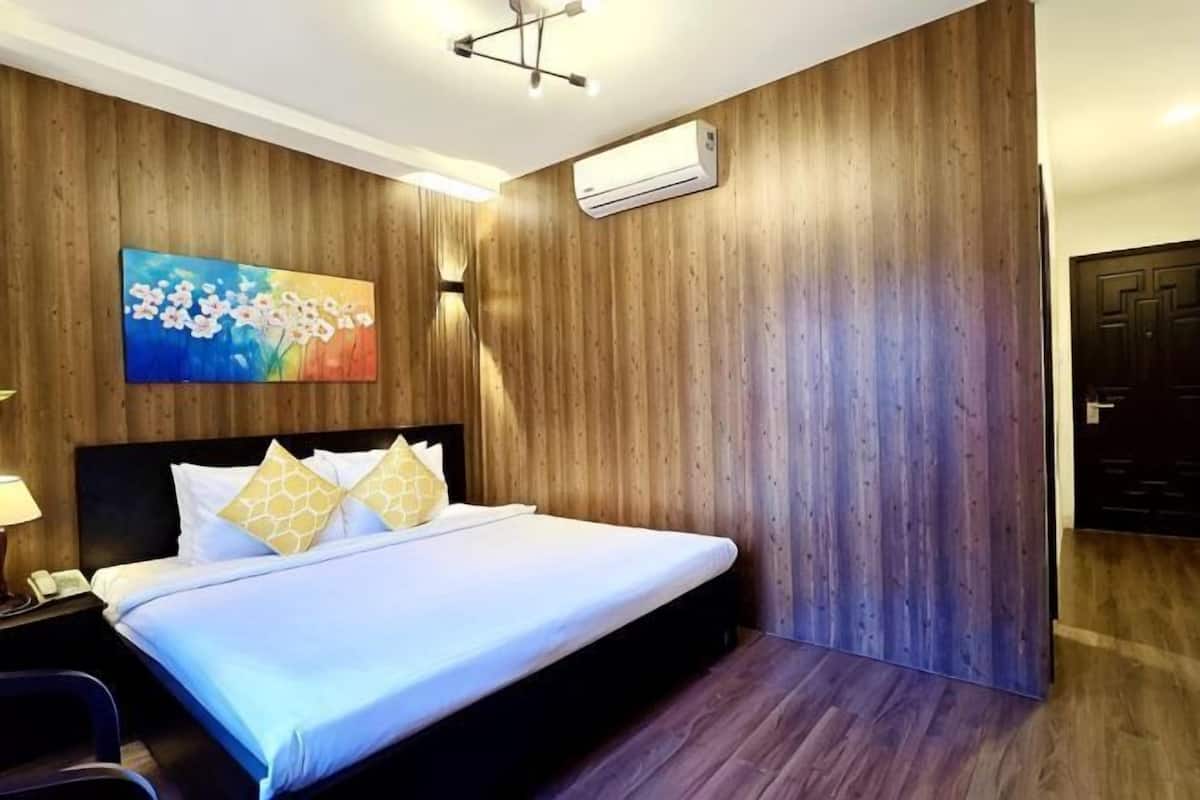 Une chambre d’hôtel avec un mur en bois, un lit agrémenté d’oreillers blancs et dorés, un tableau et un appareil de climatisation.
