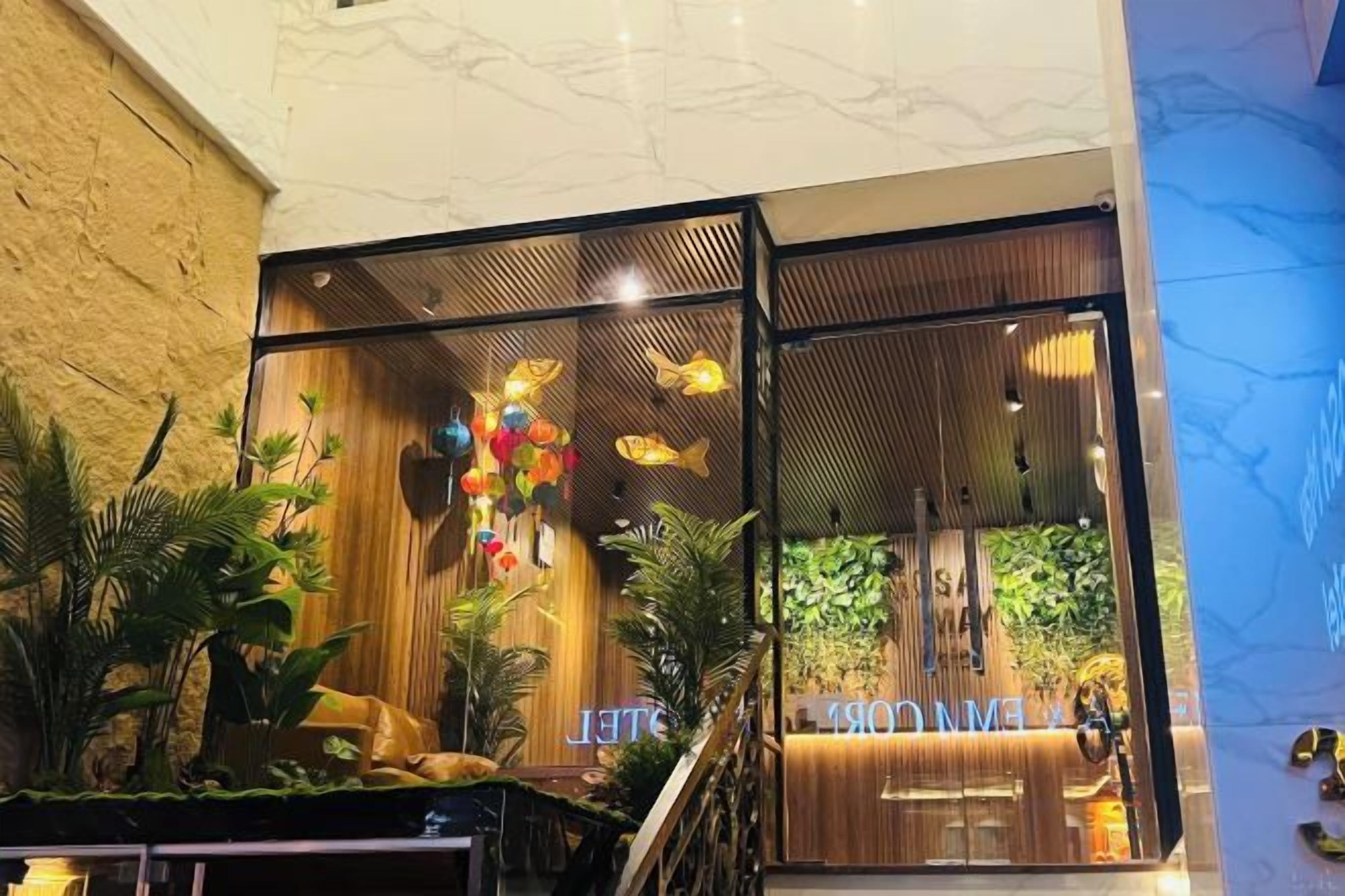 A hotel lobby with a reception desk, potted plants, and a staircase.