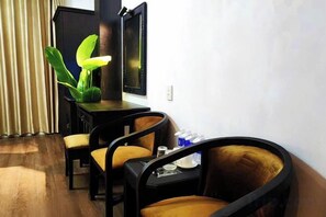 Ein Hotelzimmer mit Holzboden, einem Schreibtisch mit Stuhl, einem Fernseher und einer großen Zimmerpflanze.