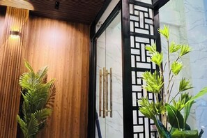 A wooden wall with a geometric black metal partition, a potted plant, and a glass door with a handle. - RosaMay Thu Khoa Huan (Ho Chi Minh City)