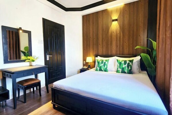 A bedroom with a large bed, a desk, a chair, a mirror, and a nightstand with a lamp.