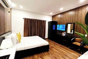 Una habitación de hotel con una cama, un escritorio con lámpara, televisión y una planta.