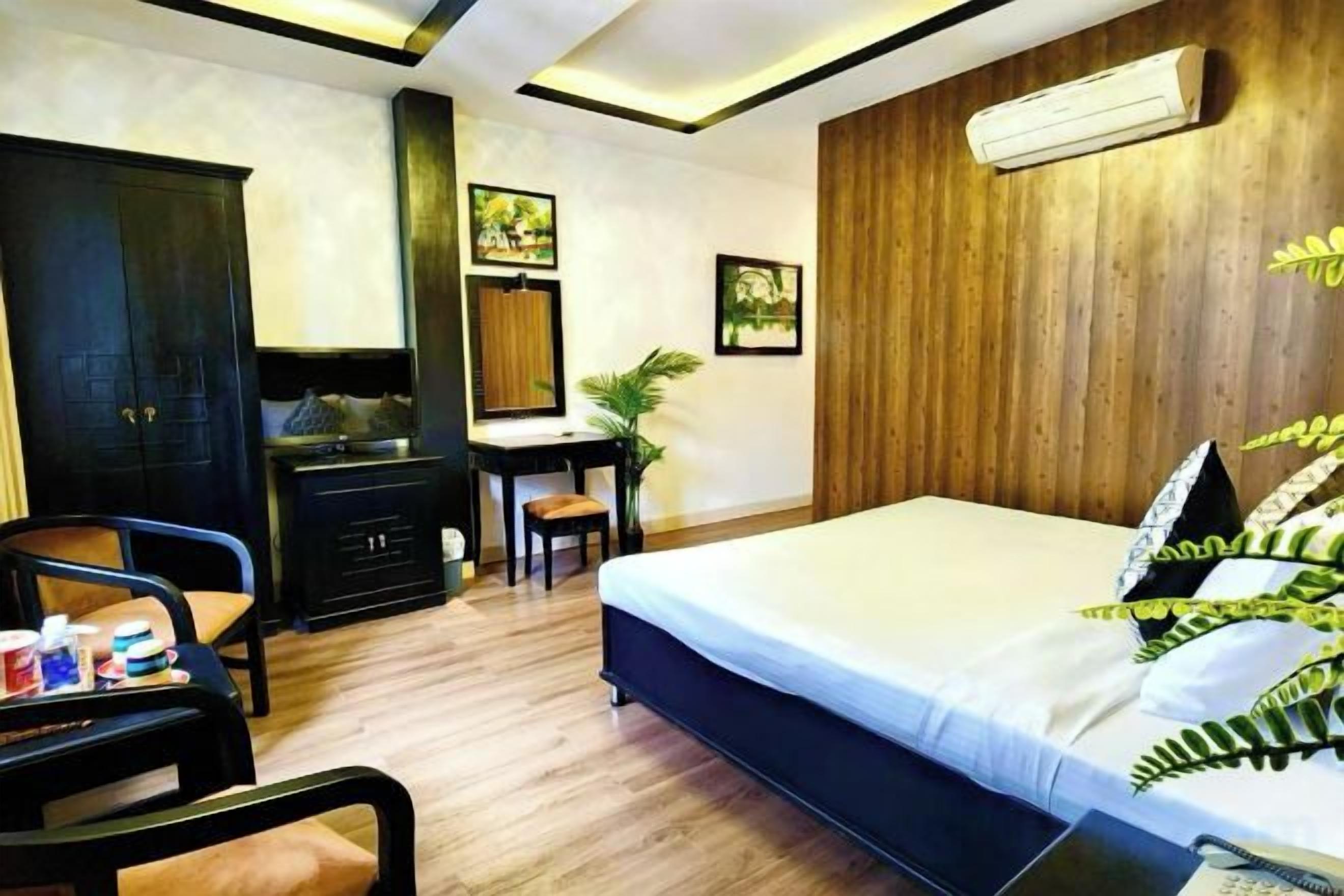 A hotel room with a bed, desk, chair, wardrobe, and a small table with a plant.