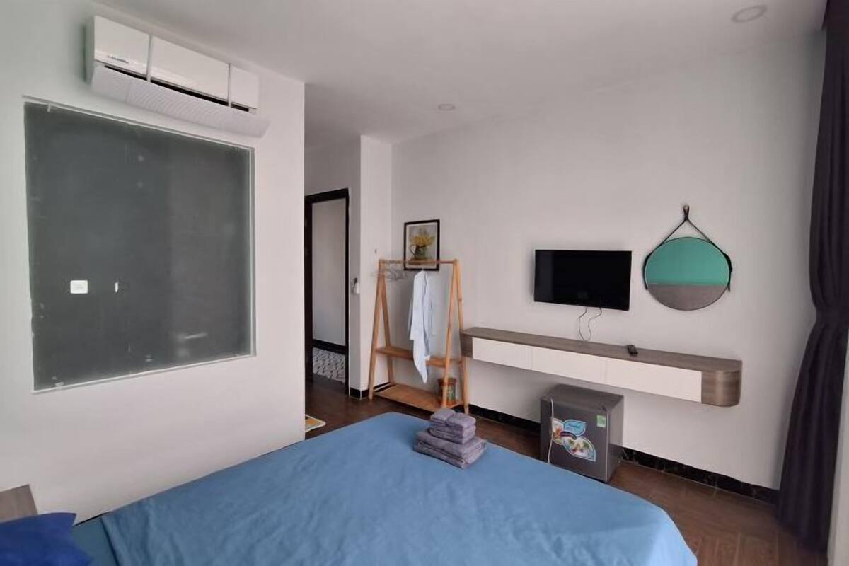 A bedroom with a bed, a TV, a wall-mounted shelf, and a window.