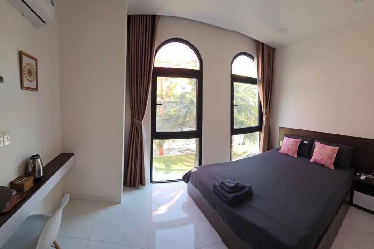 A bedroom with a bed, a desk, and two windows with curtains.