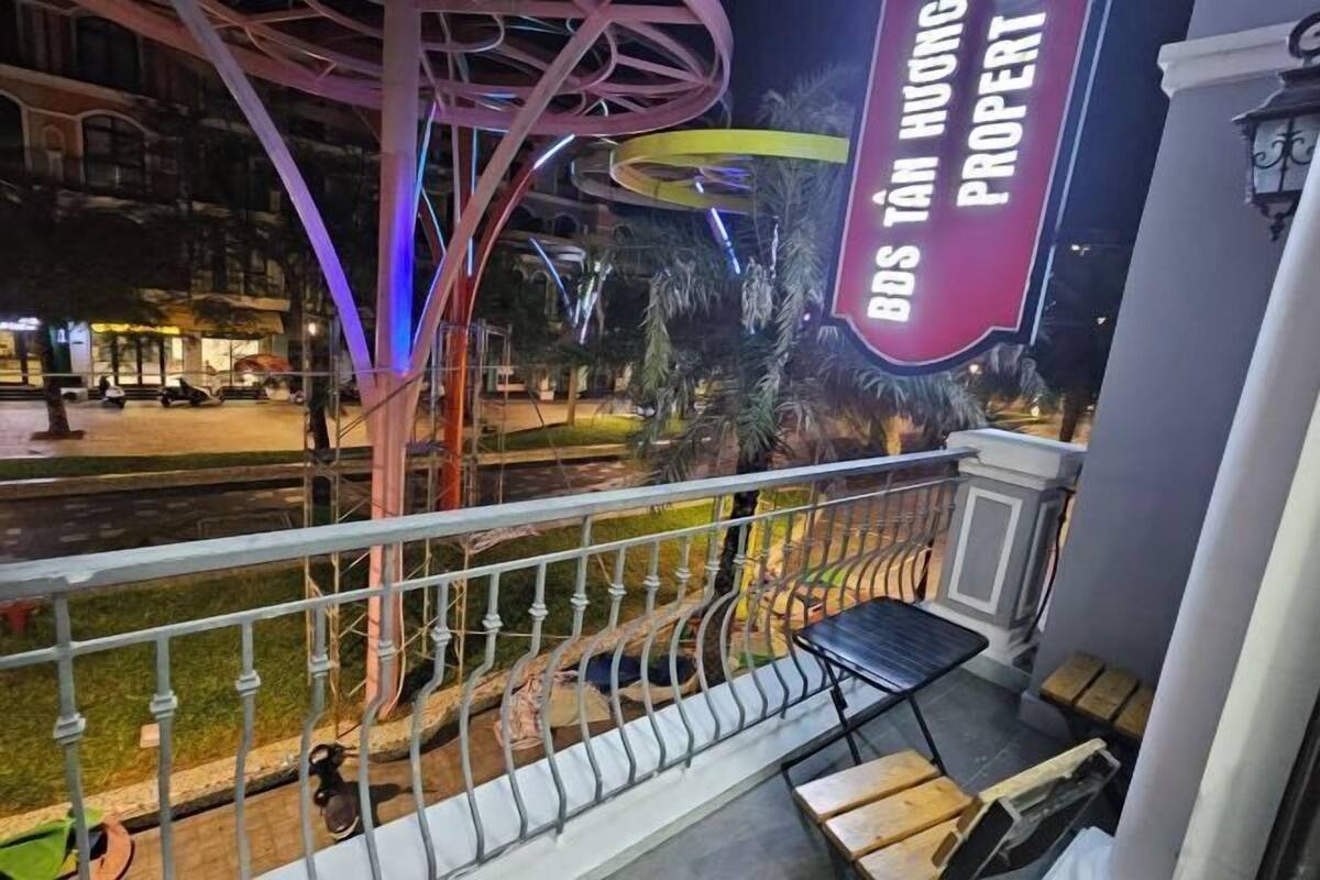 A balcony with a view of a street, a metal railing, and a sign for 'BDS TAN HUONG PROPERTY'.