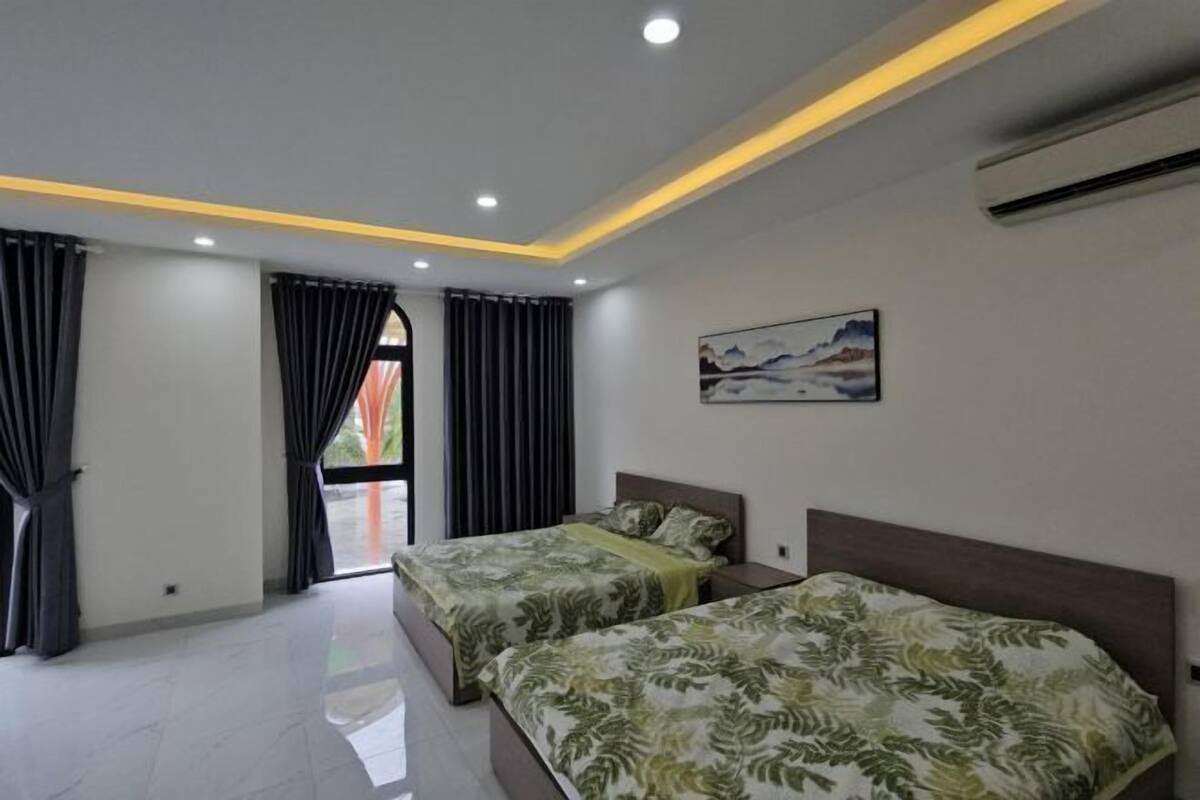 A modern hotel room with two beds, a large window with curtains, a painting on the wall, and an air conditioning unit.