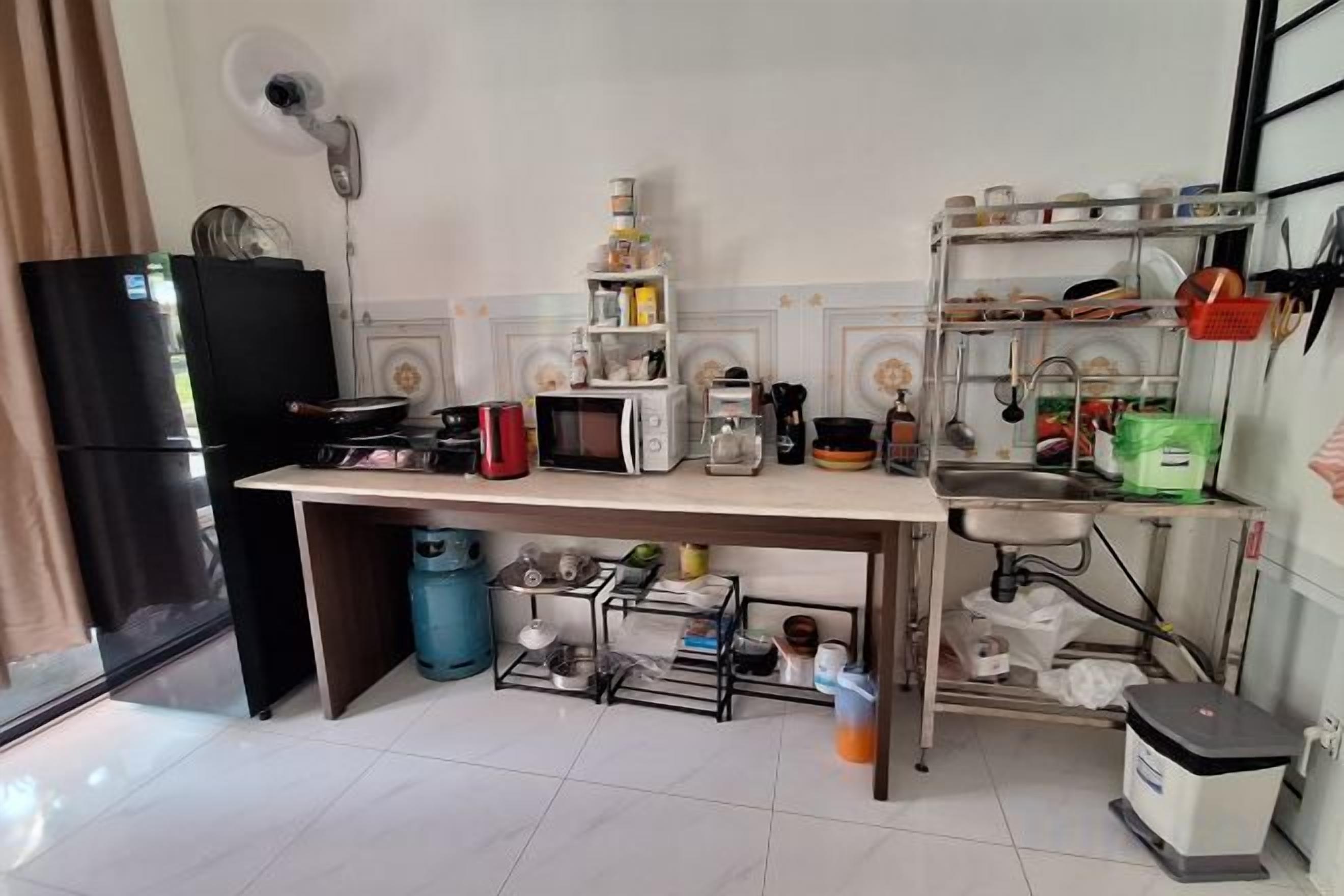 Una cocina compacta con estufa a gas, microondas y varios electrodomésticos. Cuenta con un lavamanos con grifo, un refrigerador pequeño y un estante con utensilios de cocina.