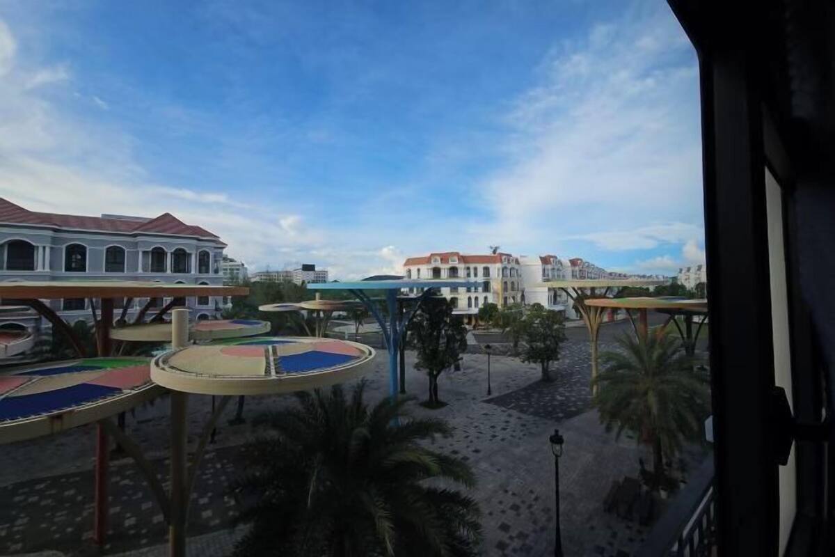 A courtyard with a playground, palm trees, and buildings in the background.
