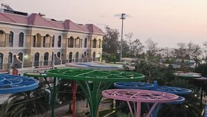 Un bâtiment doté de fenêtres en arc de cercle et d’un toit rouge, entouré d’espaces de détente en plein air avec des tables vertes et bleues.