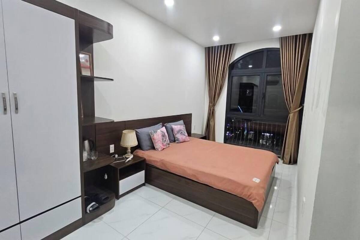 A bedroom with a bed, nightstands, a wardrobe, and a window with curtains.