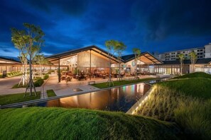 A modern hotel with a spacious lobby, outdoor seating, and a reflective pool.