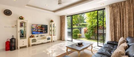 A modern living room with a sofa, a coffee table, a TV, and a sliding glass door leading to a garden.