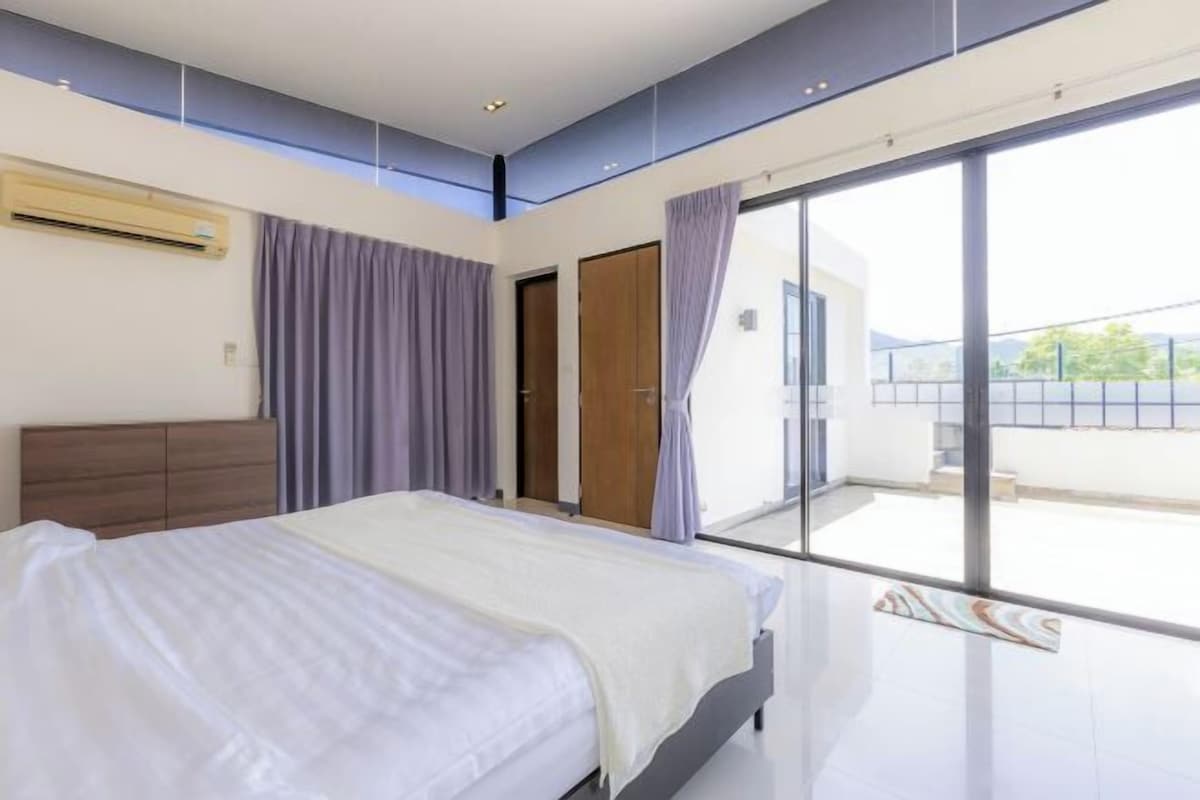 Un dormitorio moderno con una cama grande, puertas de cristal correderas a un balcón y aire acondicionado integrado.