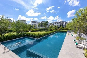 A swimming pool with a clear blue sky, surrounded by greenery and modern buildings.