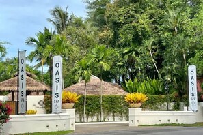 A resort entrance with 'OASIS SPA' signs, surrounded by tropical vegetation and thatched-roof structures.
