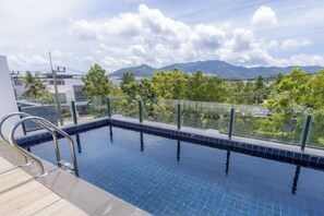 A swimming pool with a metal ladder, surrounded by a glass fence, with a view of mountains and greenery in the background. - Five bedroom Laguna Park Side Villa - Triple 8 Asia (Phuket)