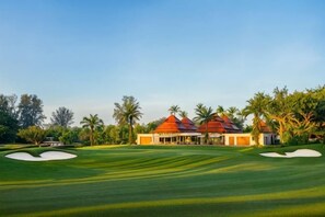 A golf course with a clubhouse, palm trees, and a clear sky.