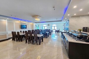 Un comedor amplio con varias mesas y sillas, un mostrador de buffet y grandes ventanales que ofrecen luz natural.