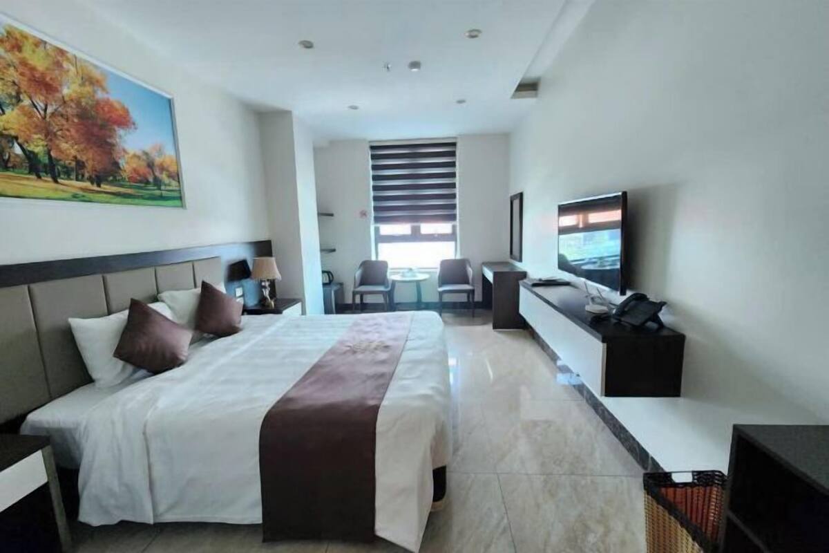 A hotel room with a bed, a desk, a TV, and a painting on the wall.