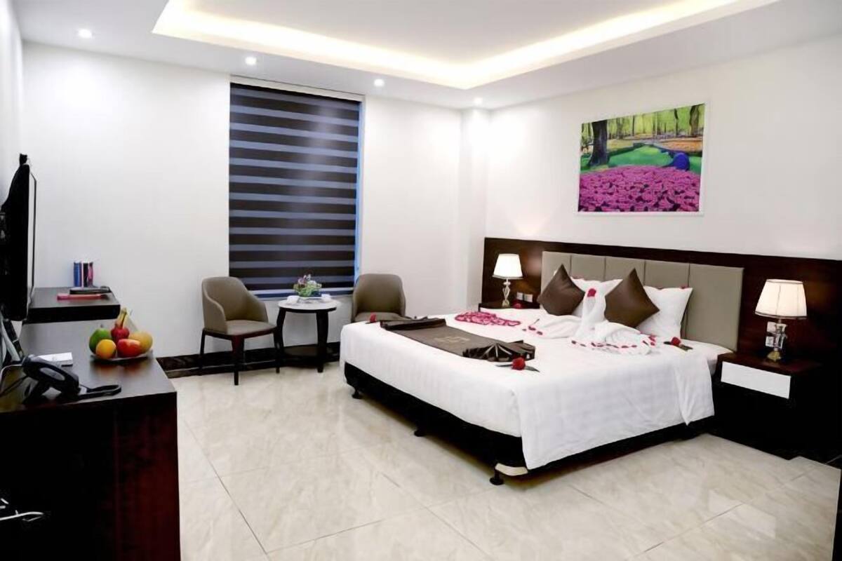 A hotel room with a bed, two chairs, a desk, a TV, and a window with blinds.
