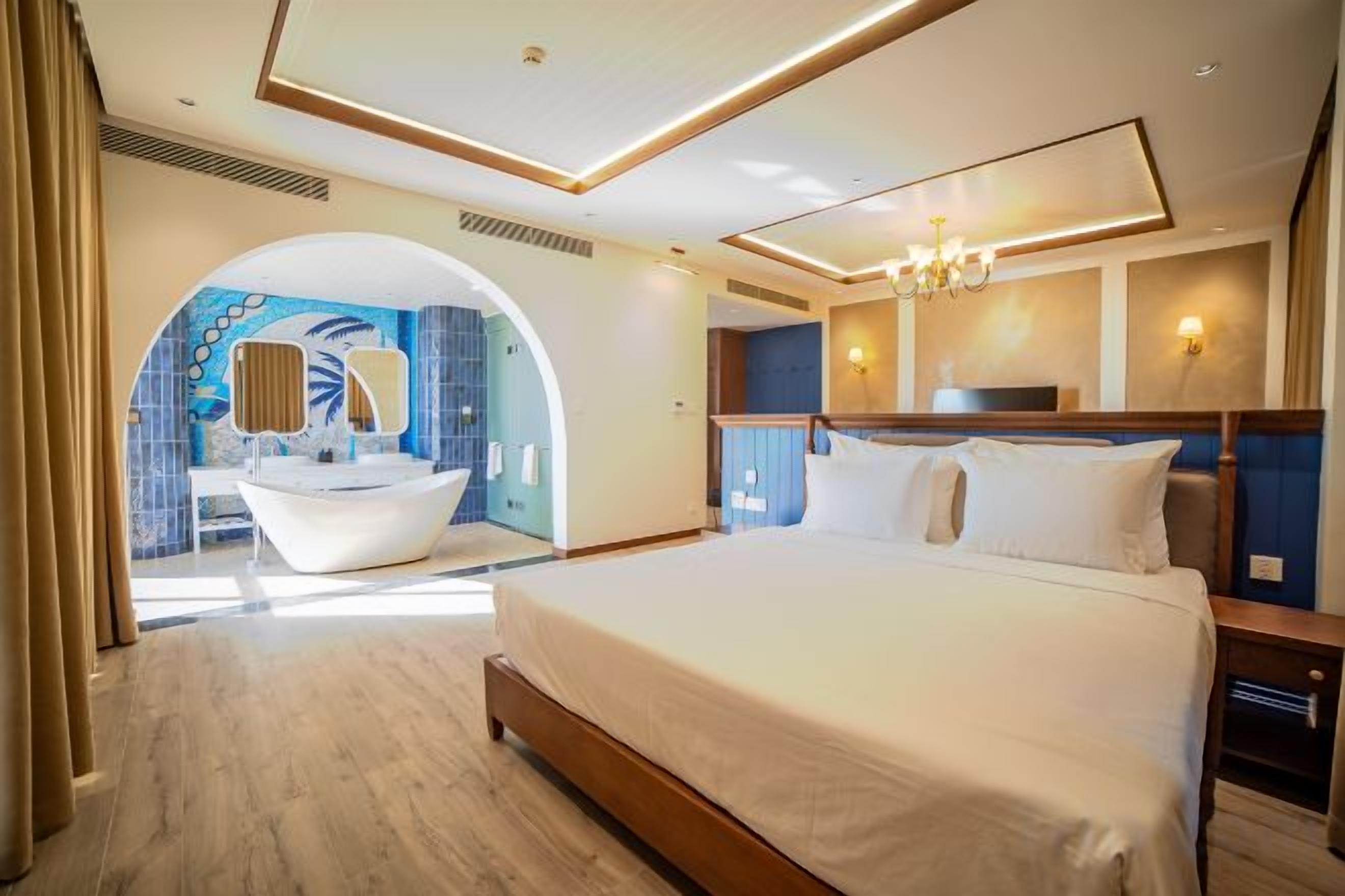 Habitación de hotel con una cama grande, baño con bañera y vista a través de un arco.