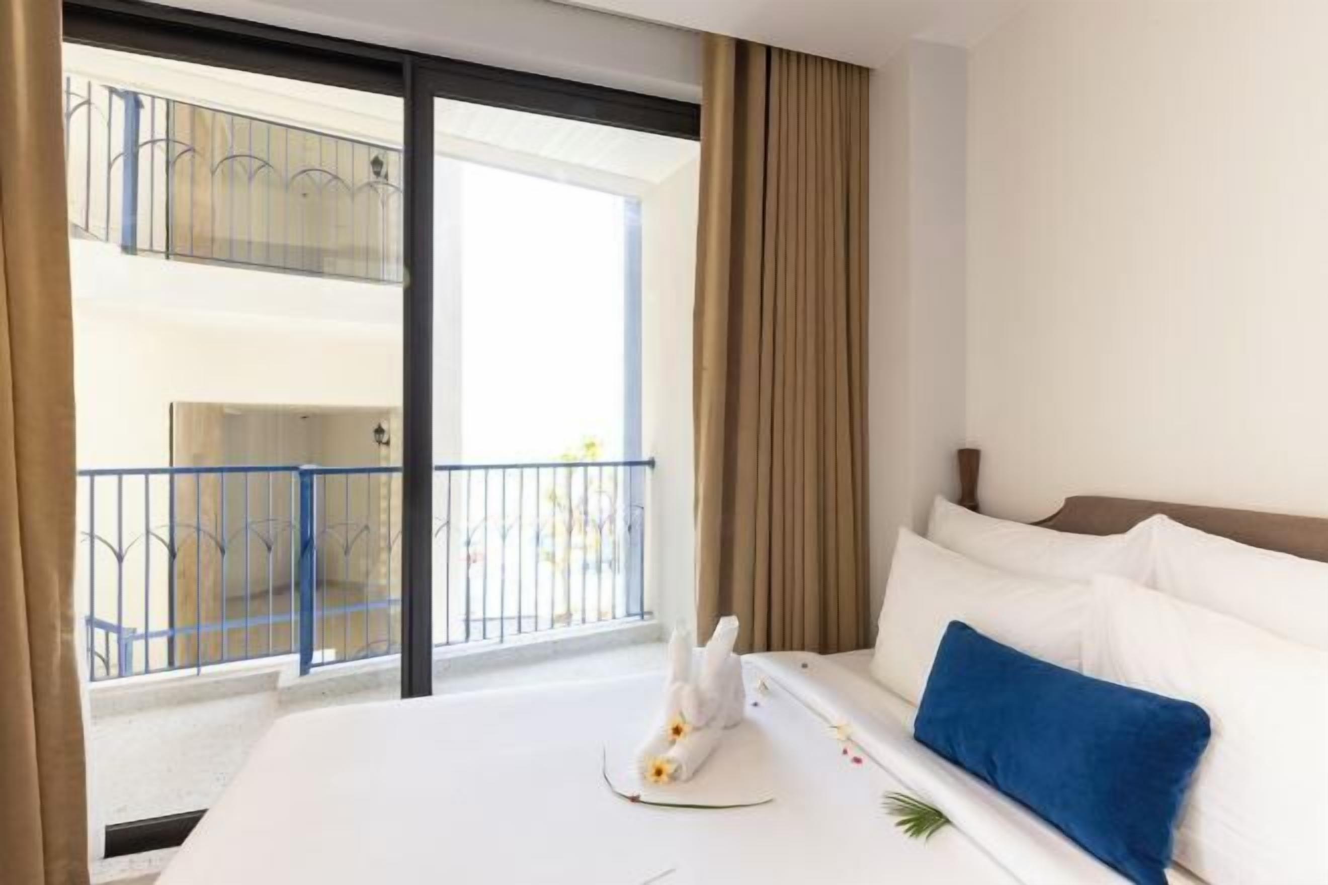 A hotel room with a bed, a view of a balcony with a railing, and a window with curtains.