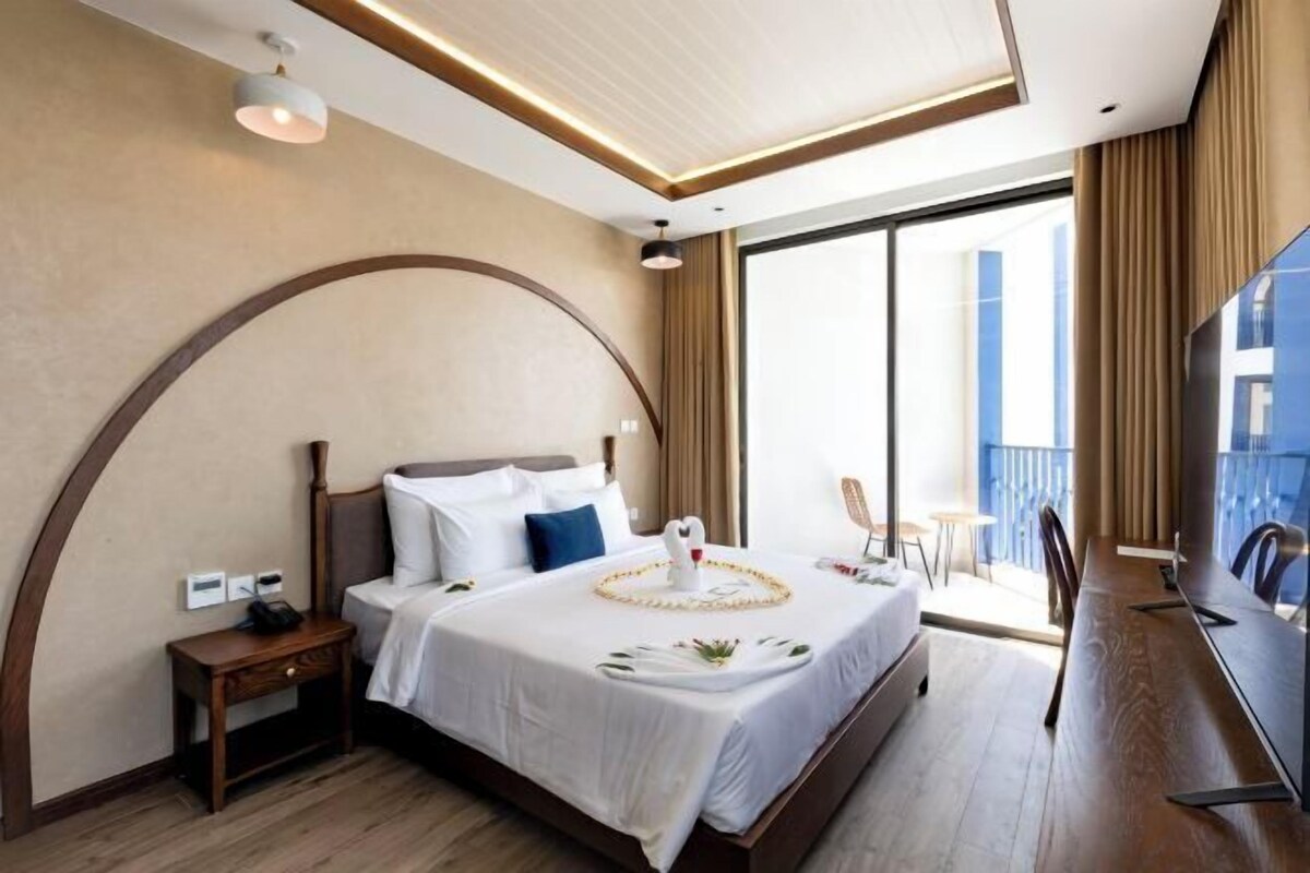 A hotel room with a large bed, a desk, a chair, and a balcony with a view.