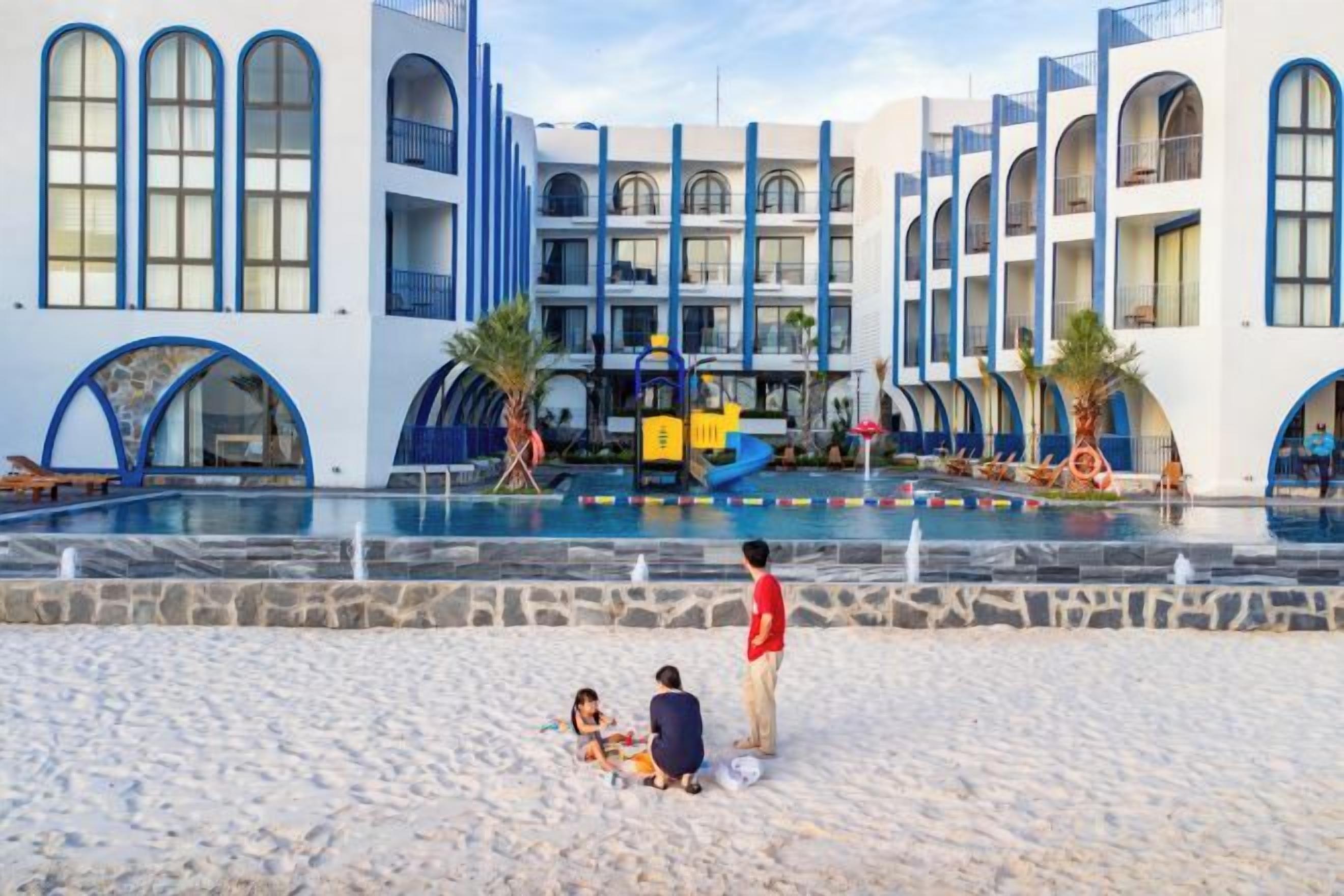 Un hotel con zona de piscina, varios balcones y una playa de arena.