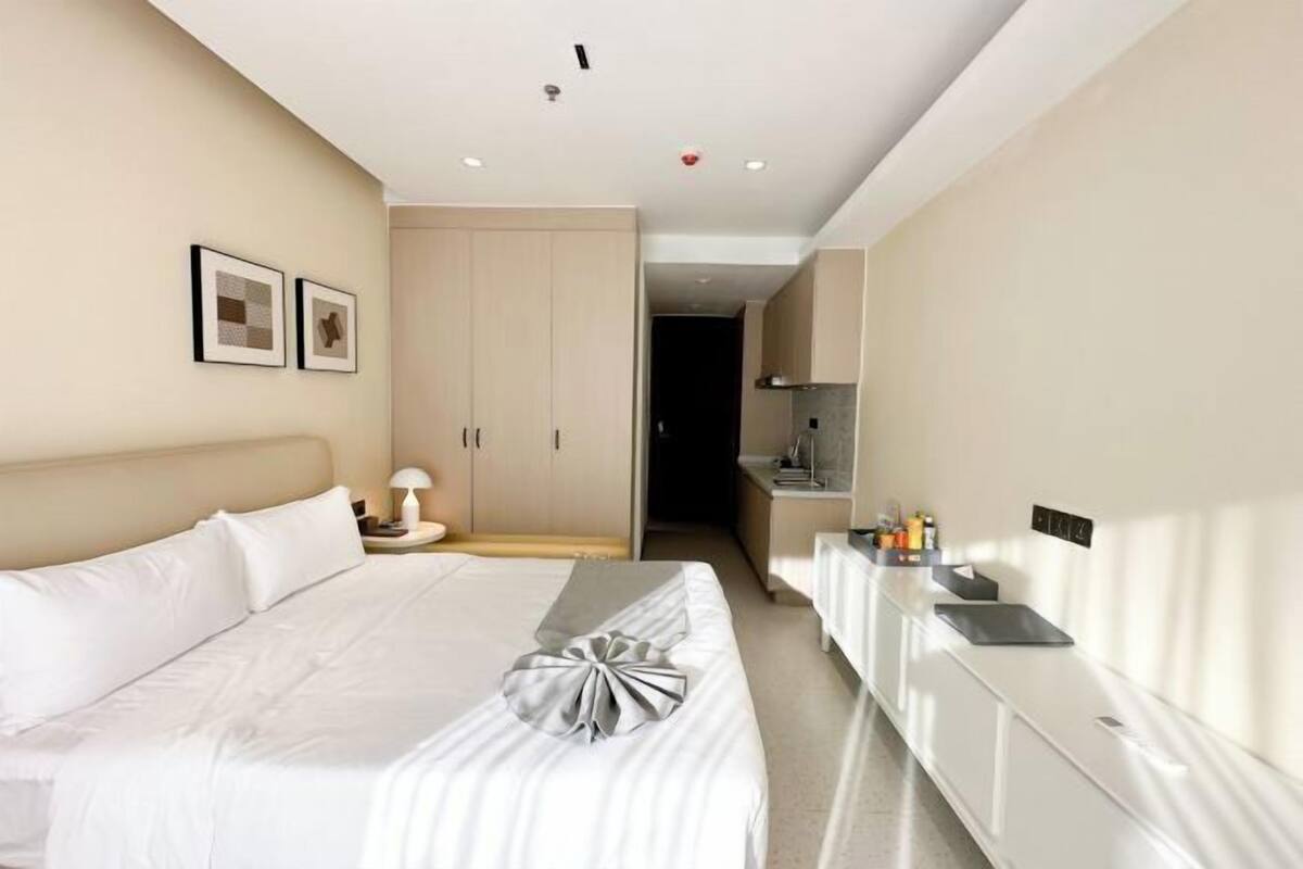 Een hotelkamer met een bed, nachtkastje, bureau en kitchenette.