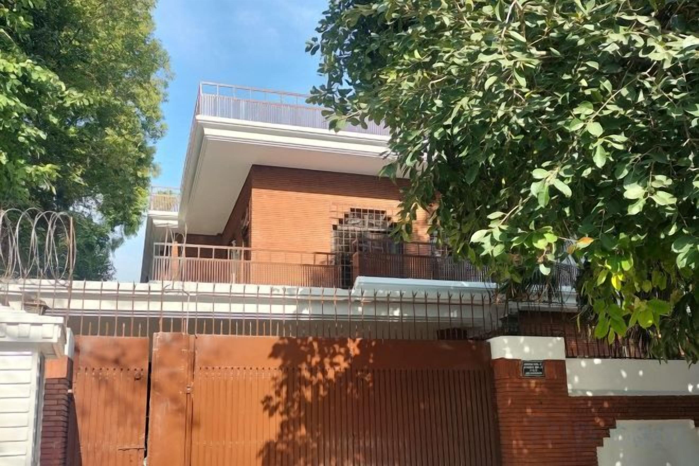 Ein zweistöckiges Gebäude mit einem Vorgeländer, einem Balkon im oberen Geschoss und einem Baum im Vordergrund.