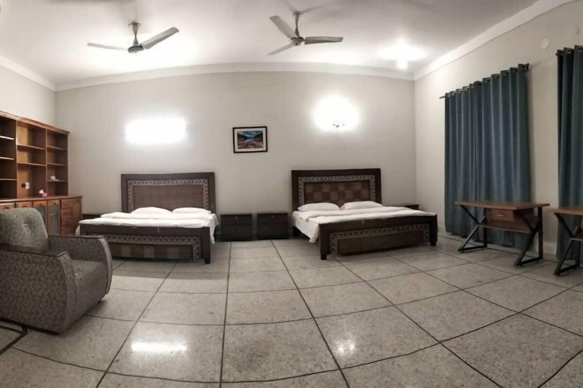 A room with two beds, a chair, a desk, and ceiling fans.