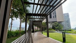 A covered walkway with a bench, surrounded by greenery and a view of modern buildings. - Axon Residence Kuala Lumpur KLCC Pavillion BB (Kuala Lumpur)