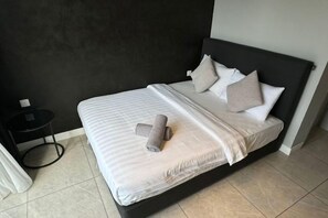 Una cama con colchón blanco, cabecera negra y varias almohadas.