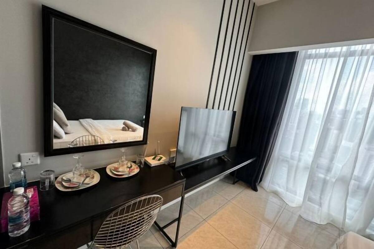 A modern hotel room with a large bed, a desk with a chair, a flat-screen TV, and a large window with sheer curtains.