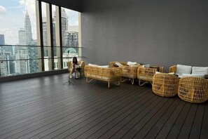 Un salón moderno con mobiliario de mimbre, ventanas amplias y vistas a un horizonte urbano.