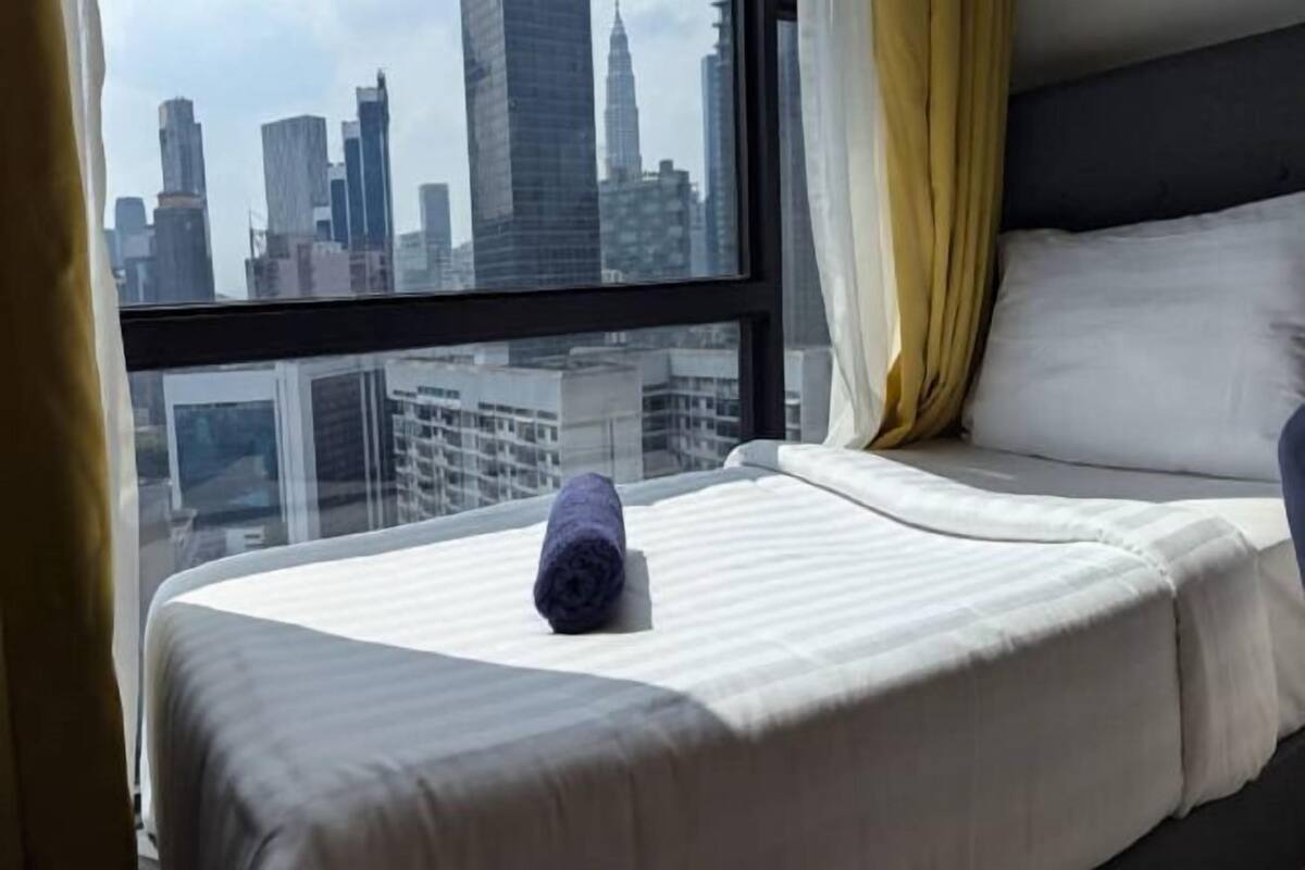 A hotel room with a bed, a window with a cityscape view, and a curtain.