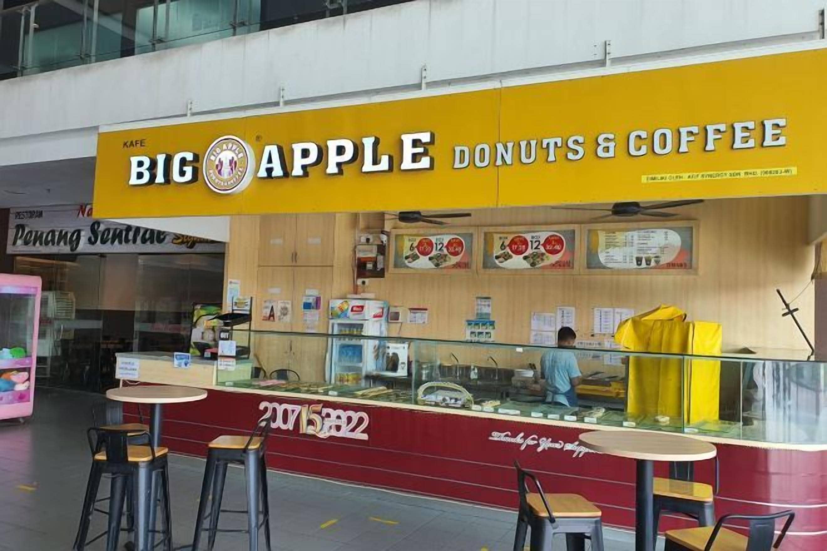 A cafe named 'Big Apple Donuts & Coffee' with a yellow sign, a counter with stools, and a menu board.