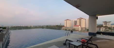 An infinity pool with a view of high-rise buildings, lounge chairs, and a covered area.