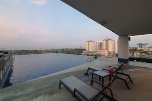 Piscina infinita com vista para edifícios altos, espreguiçadeiras e área coberta.