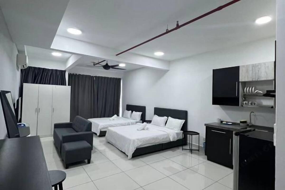 Une chambre d’hôtel moderne équipée de deux lits, d’un bureau, d’un canapé, d’une kitchenette et d’un ventilateur de plafond.
