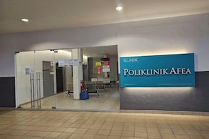 A entrada de uma clínica com uma placa indicando 'POLIKLINIK AFEA' e uma porta de vidro que dá acesso ao interior.