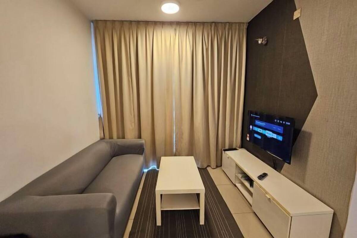 Une chambre d’hôtel avec un canapé, une petite table, un téléviseur posé sur un meuble et un rideau.