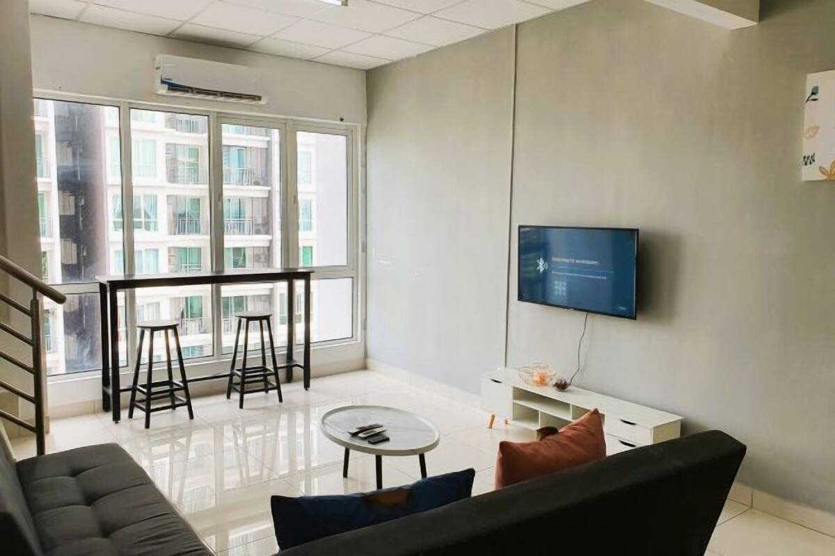 Un salon moderne avec un canapé, une table basse et un téléviseur fixé au mur. Il y a un balcon avec une balustrade et une vue sur les bâtiments environnants.