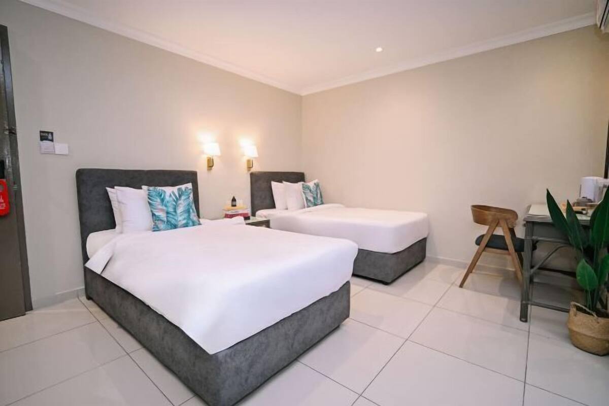 A hotel room with two beds, a desk, a chair, and a potted plant.