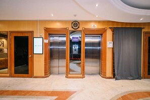 A hotel lobby with wooden doors, an elevator, and a reception area.