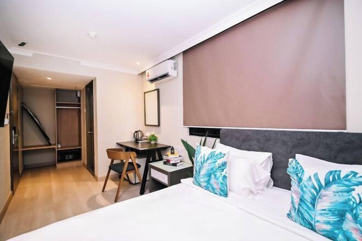 A hotel room with a bed, a desk, a chair, a wardrobe, and an air conditioning unit.